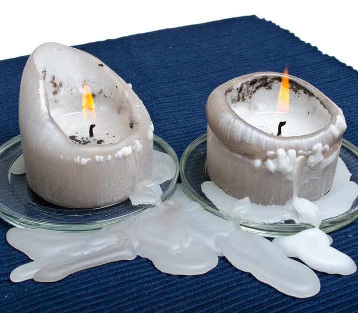 Bilden visar två brinnande ljus i grå färg som står på små glasunderlägg. Ljusen har brunnit ner en ...